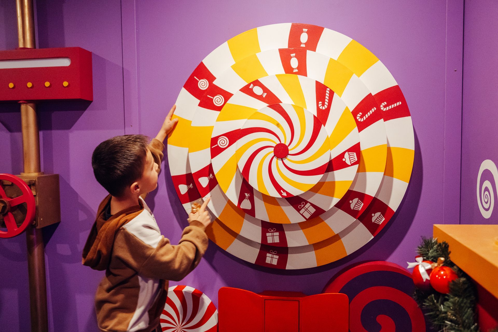 A young boy is playing with a giant lollipop on a purple wall