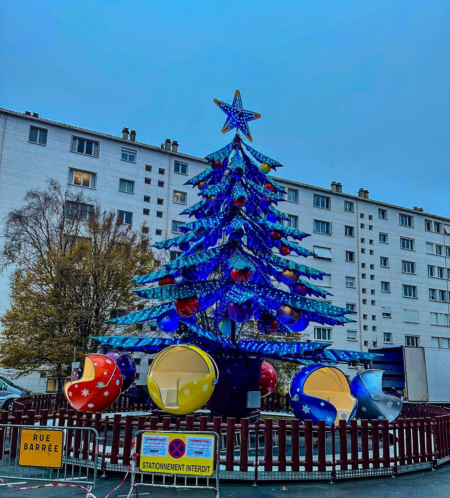 A large blue christmas tree in front of a building