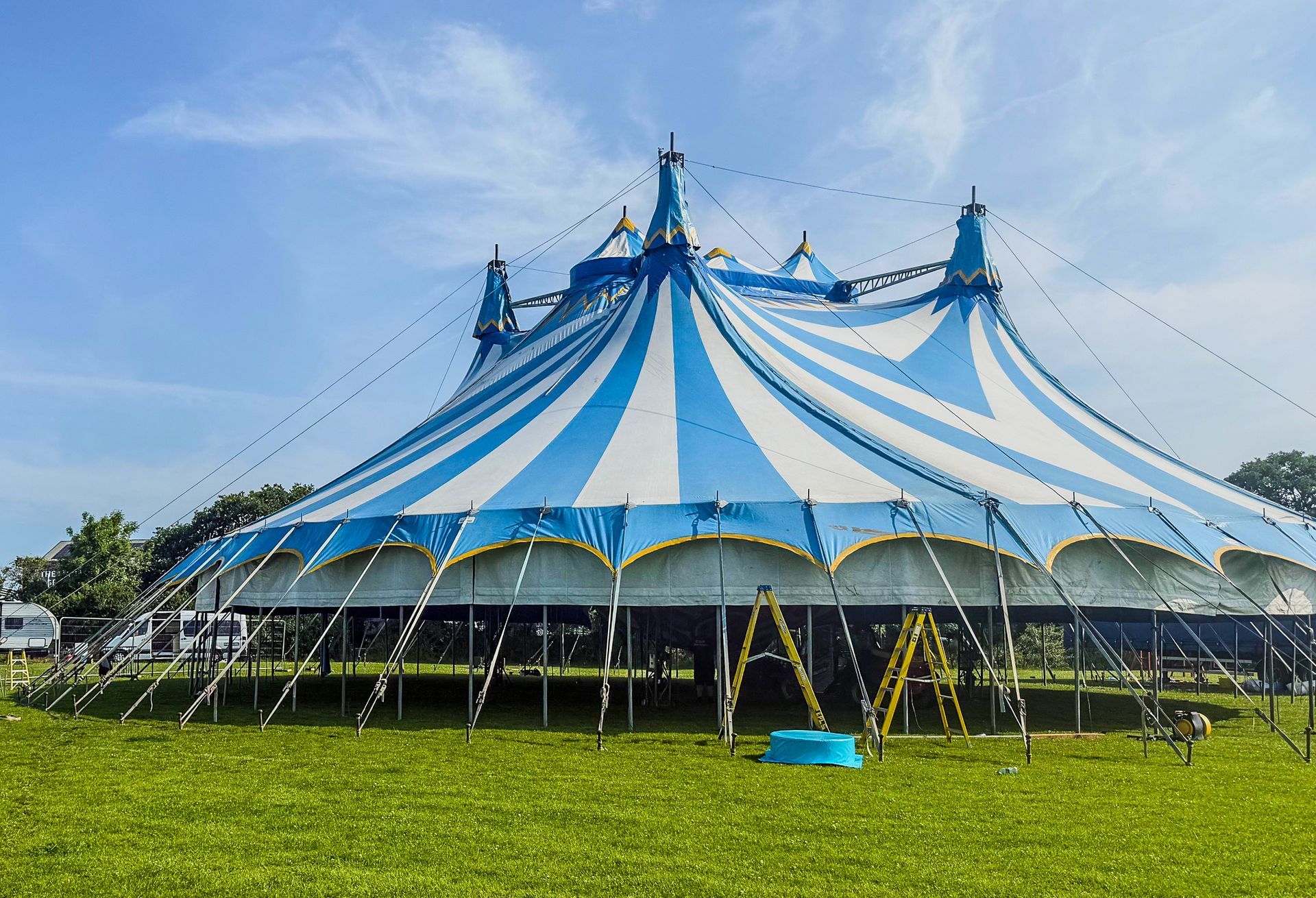 A blue and white circus tent is in the middle of a grassy field