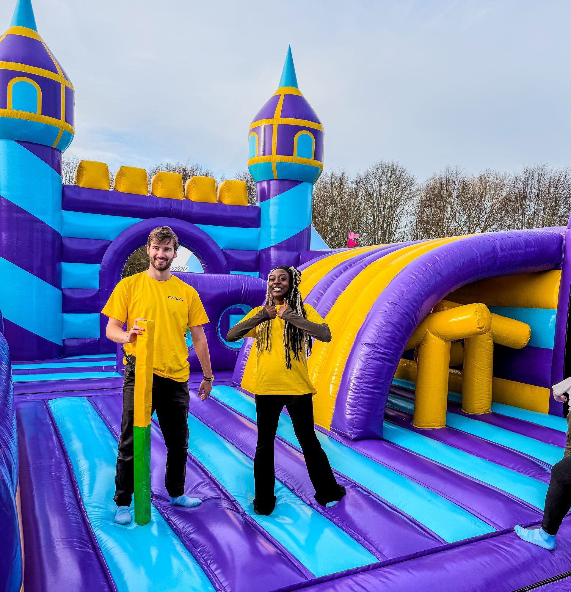 A man in a yellow shirt is standing in front of an inflatable castle