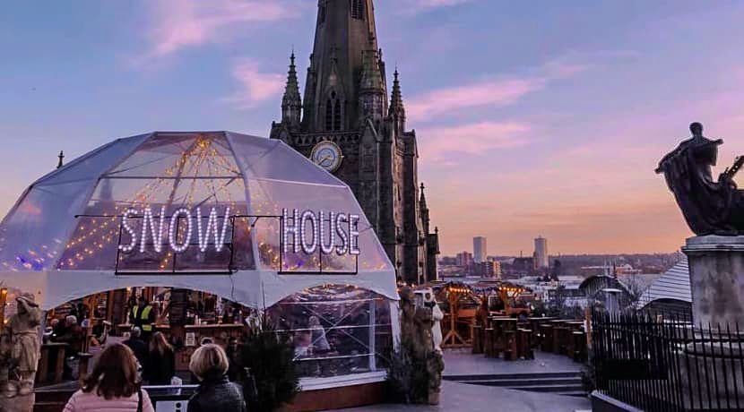 A group of people are standing in front of a dome that says snow house.