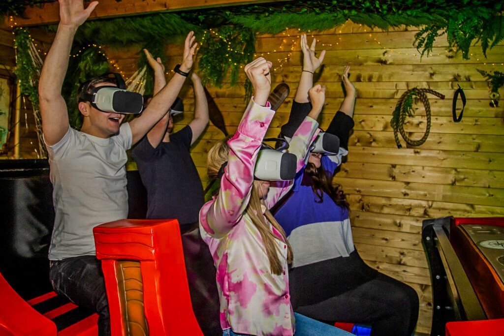 A group of people are wearing virtual reality headsets and raising their arms in the air