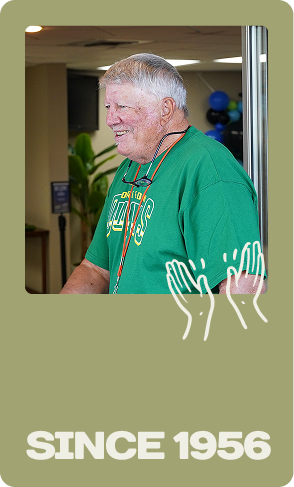 Man in green T-shirt standing indoors, with “SINCE 1956” text at the bottom