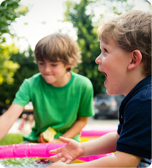 Two children playing outdoors with a bright pink toy, one laughing in the foreground