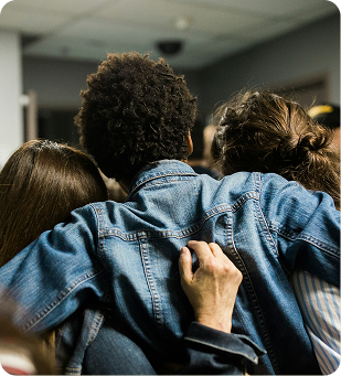 Person in a denim jacket being embraced by two others indoors