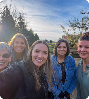 Five women smiling outdoors at sunset in a grassy field