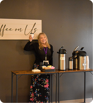 Woman smiling and holding a cup beside a coffee station with thermoses and pastries