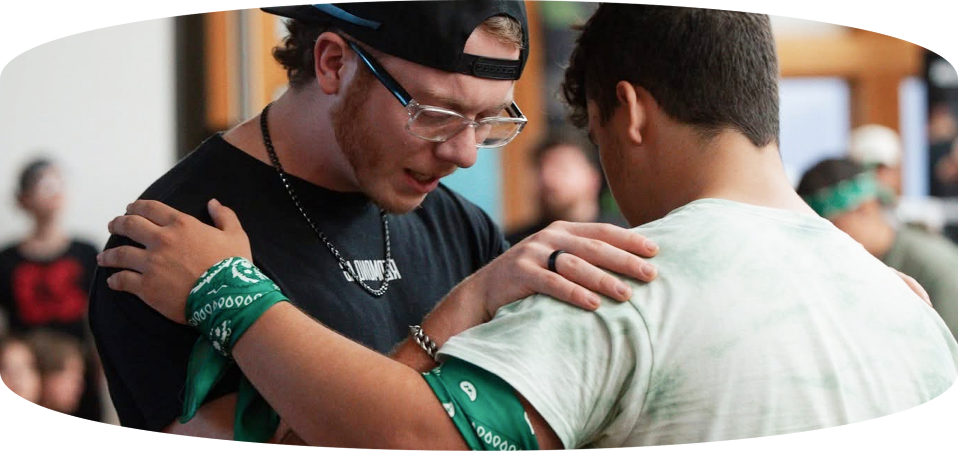 Two people in green wristbands embrace in a crowded indoor setting