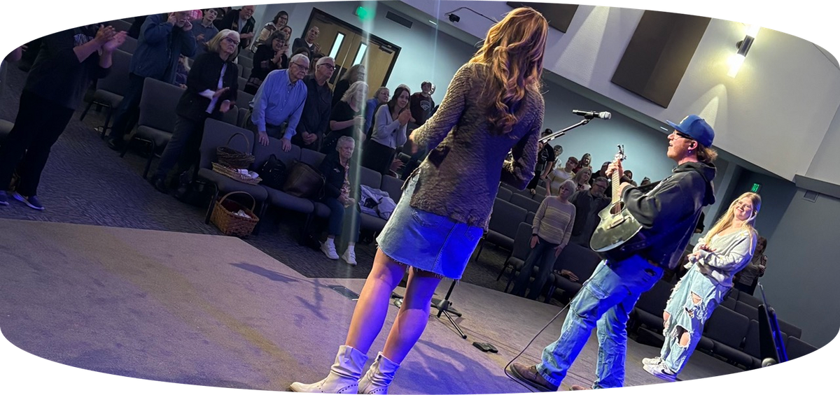 Person singing on stage with blue lighting while audience watches nearby