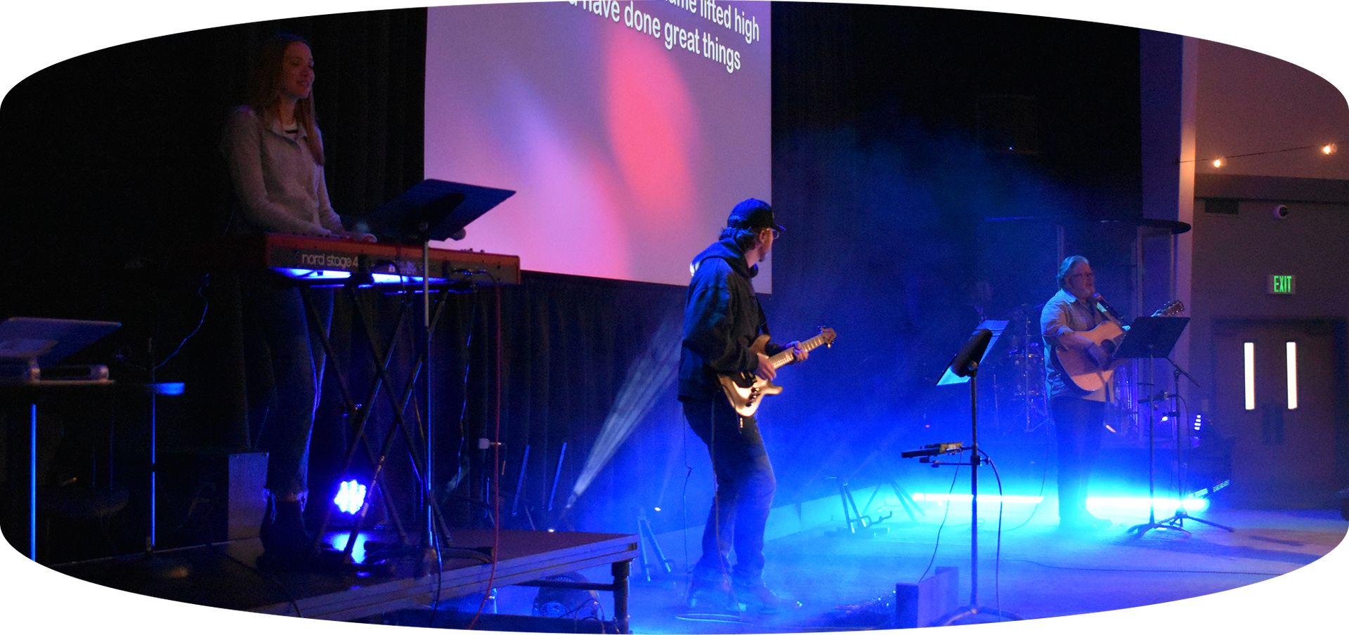 Blue-lit live band performing on stage with keyboards, guitar, and microphones
