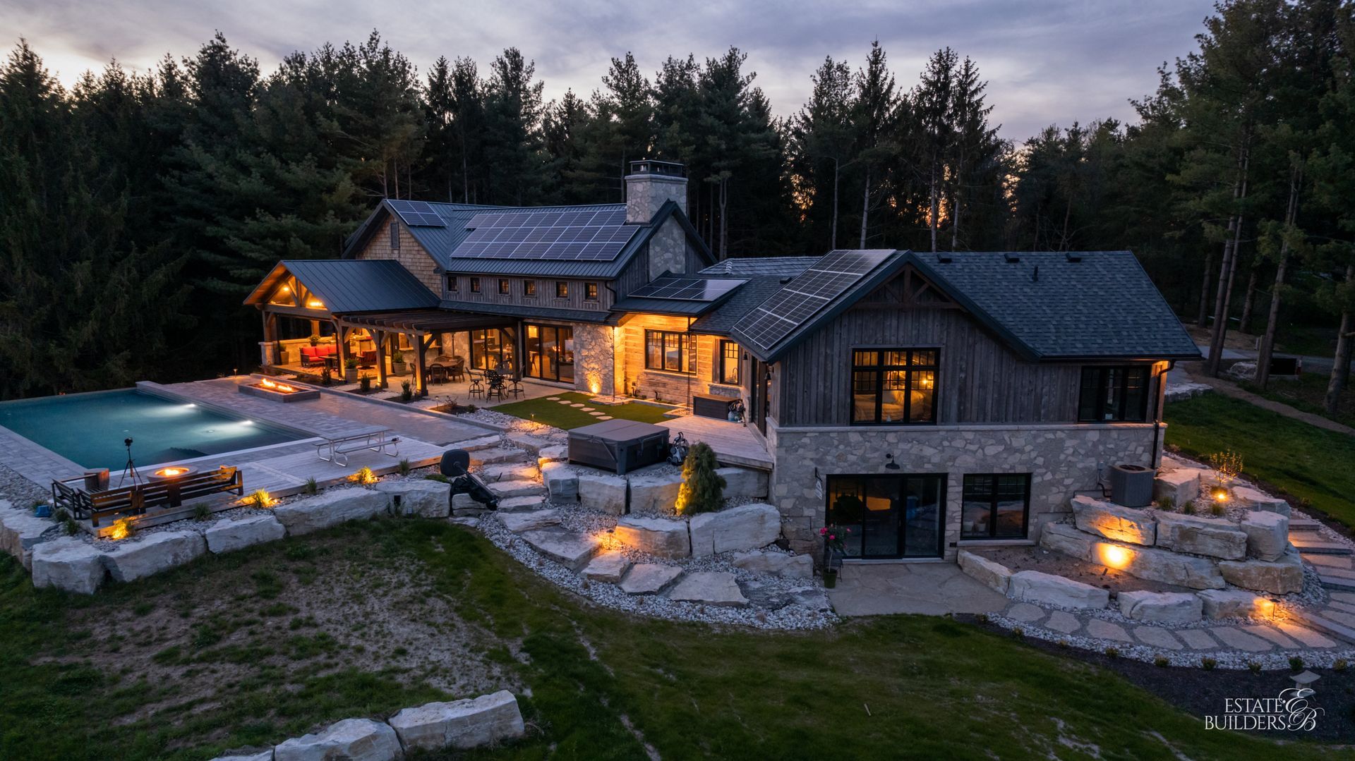 An aerial view of a large timber frame house with a pool in the backyard surrounded by trees.