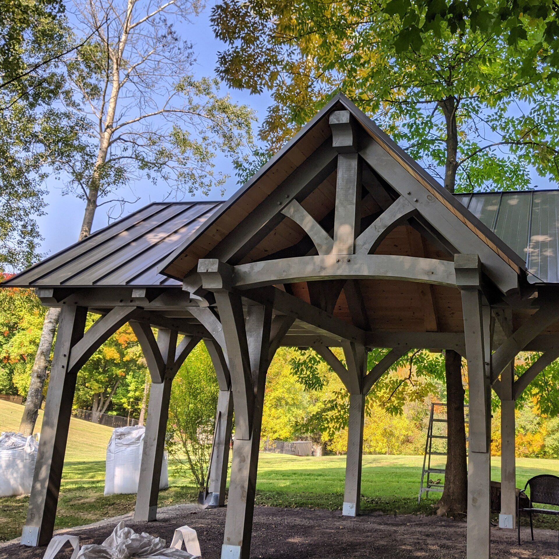 A wooden timber frame structure with a metal roof is surrounded by trees
