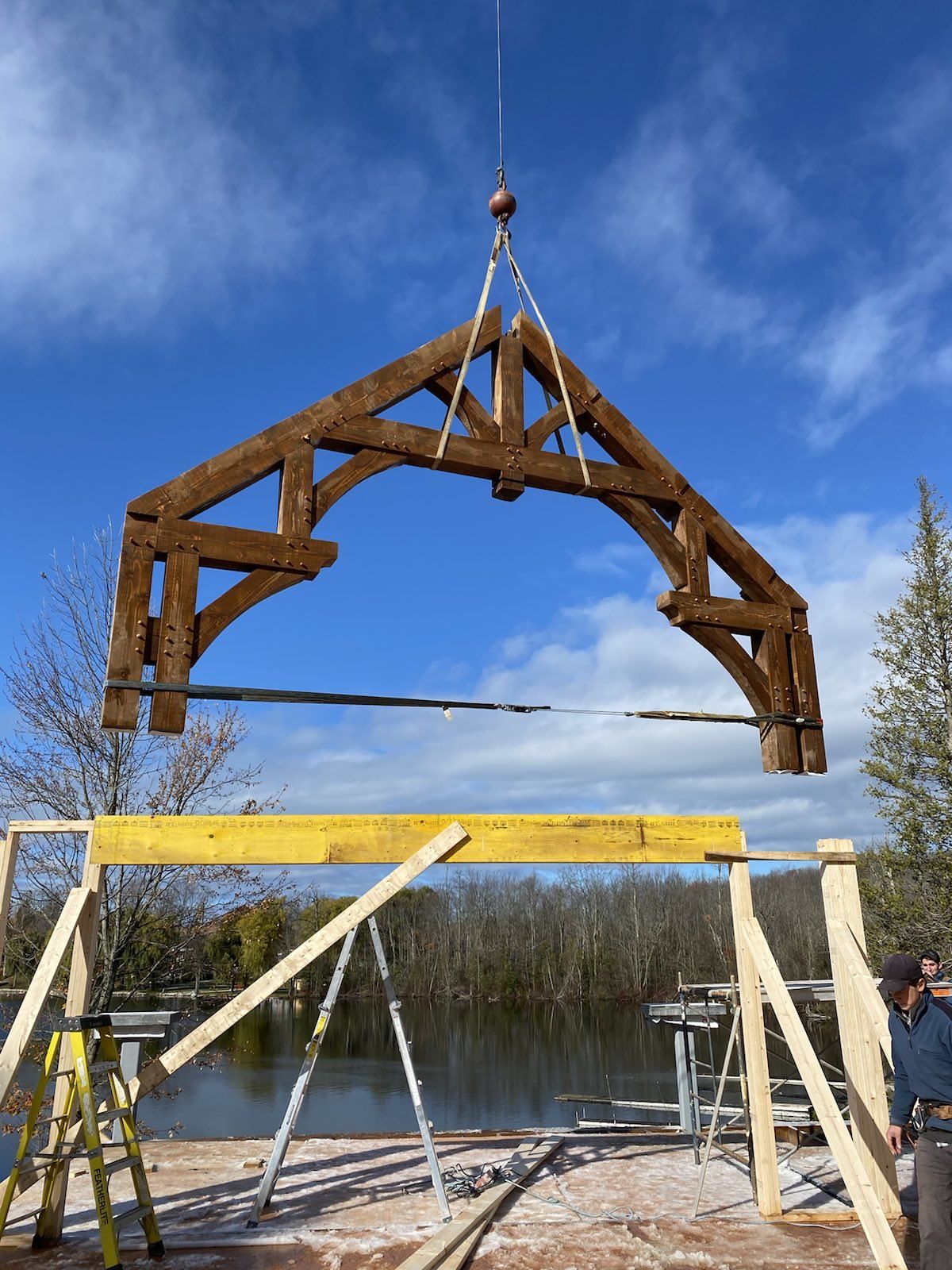 A large timber frame wooden structure is being lifted by a crane.