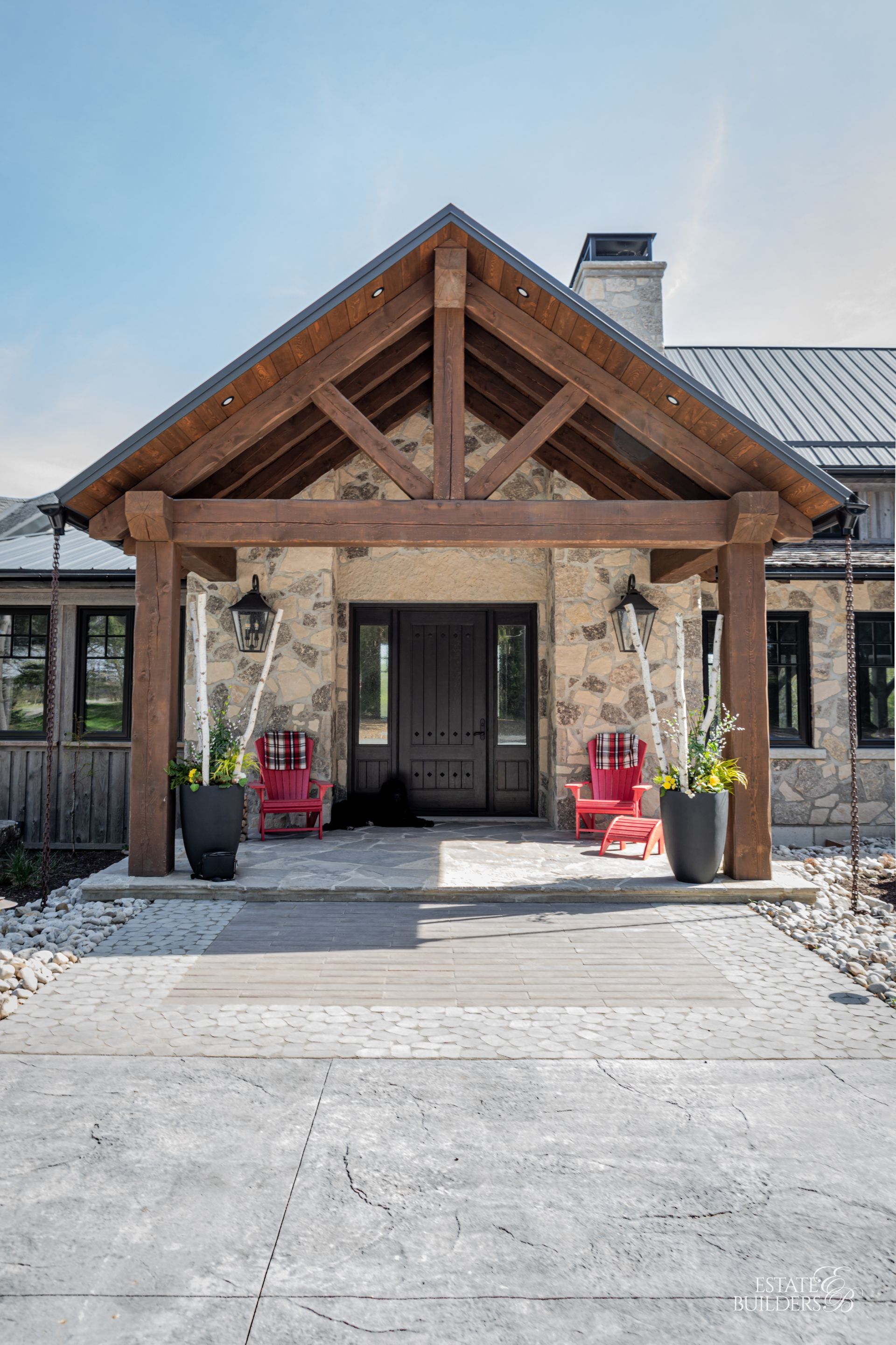 The front of a house with a wooden timber frame porch and red chairs.