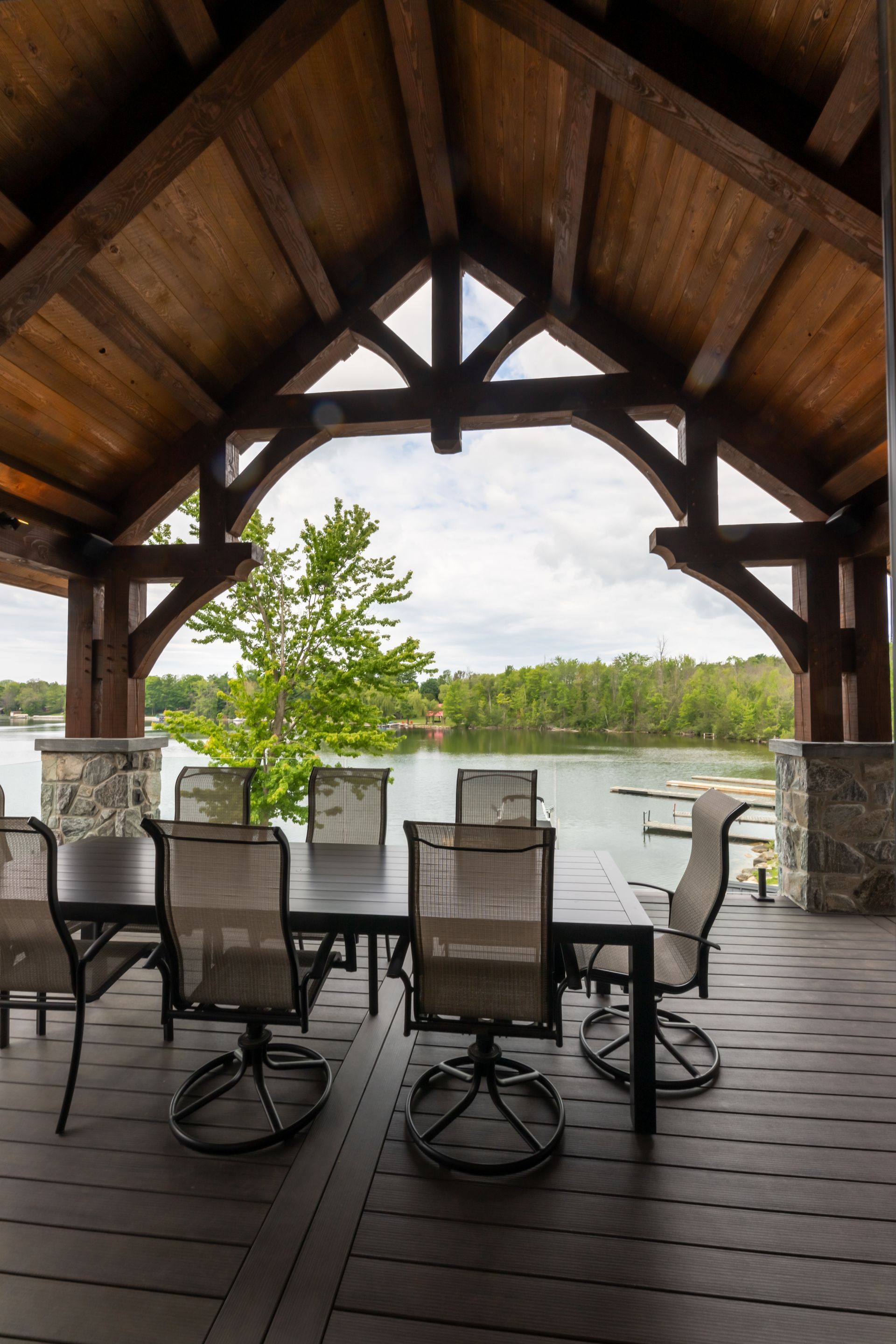 A timber frame gazebo with a table and chairs overlooking a lake.