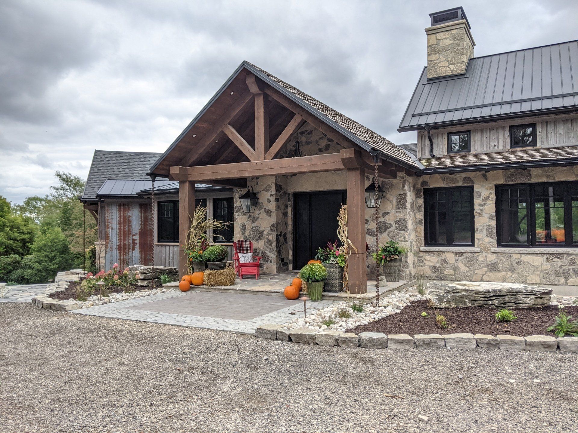 A large stone house with a timber frame porch and pumpkins in front of it.
