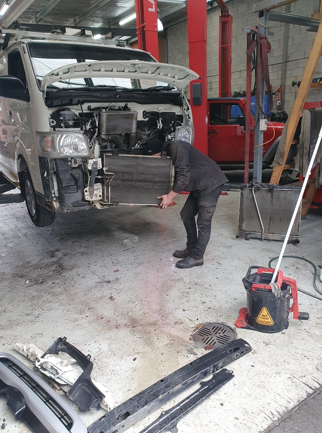 Mechanic working on the front of a van in a repair shop; hood open. Shop is messy. — COOTA Automotive Services in Ballarat East, VIC