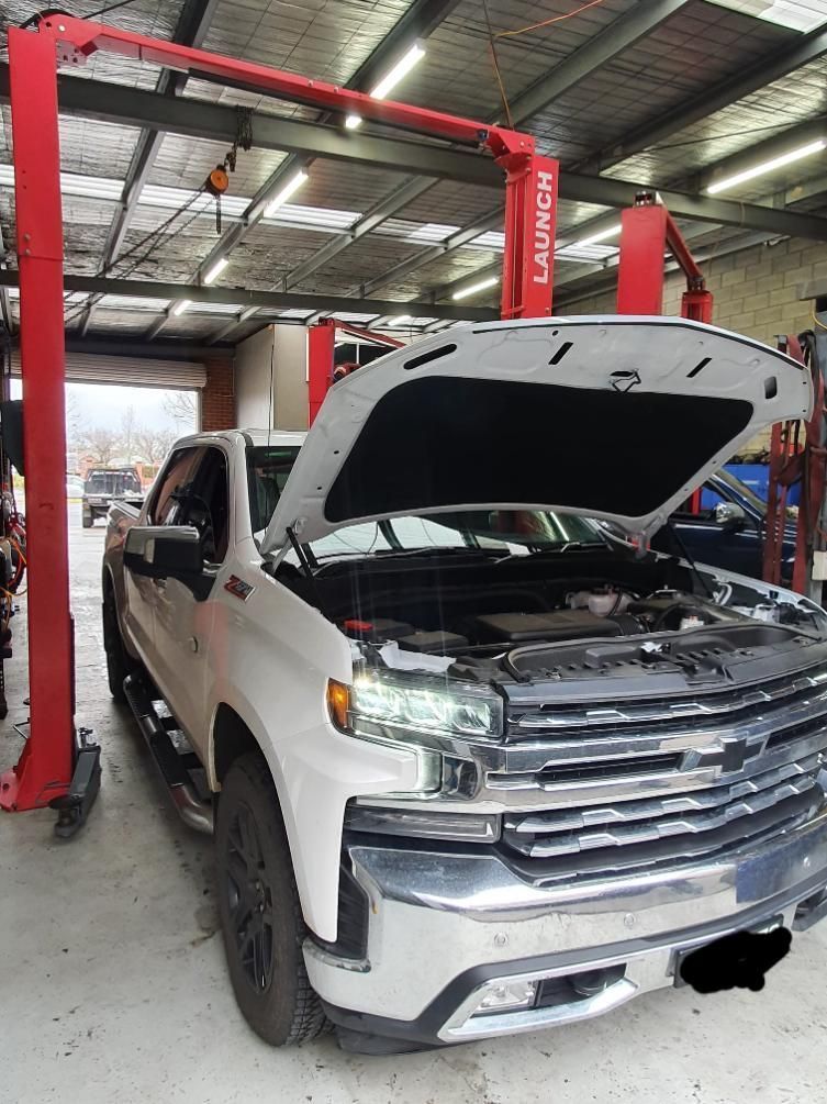 White pickup truck in a repair shop with the hood open, under a red Launch hoist — COOTA Automotive Services in Ballarat East, VIC