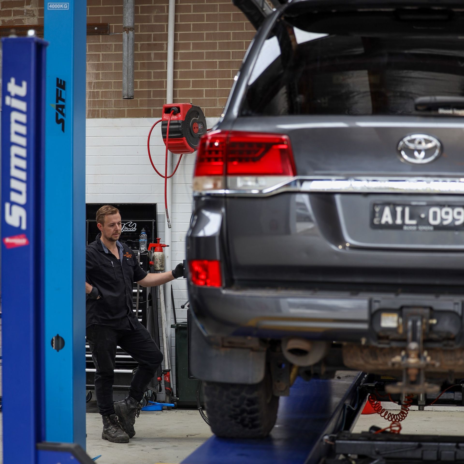 Mechanic in black uniform leaning near a gray SUV on a lift in a garage. — COOTA Automotive Services in Ballarat East, VIC