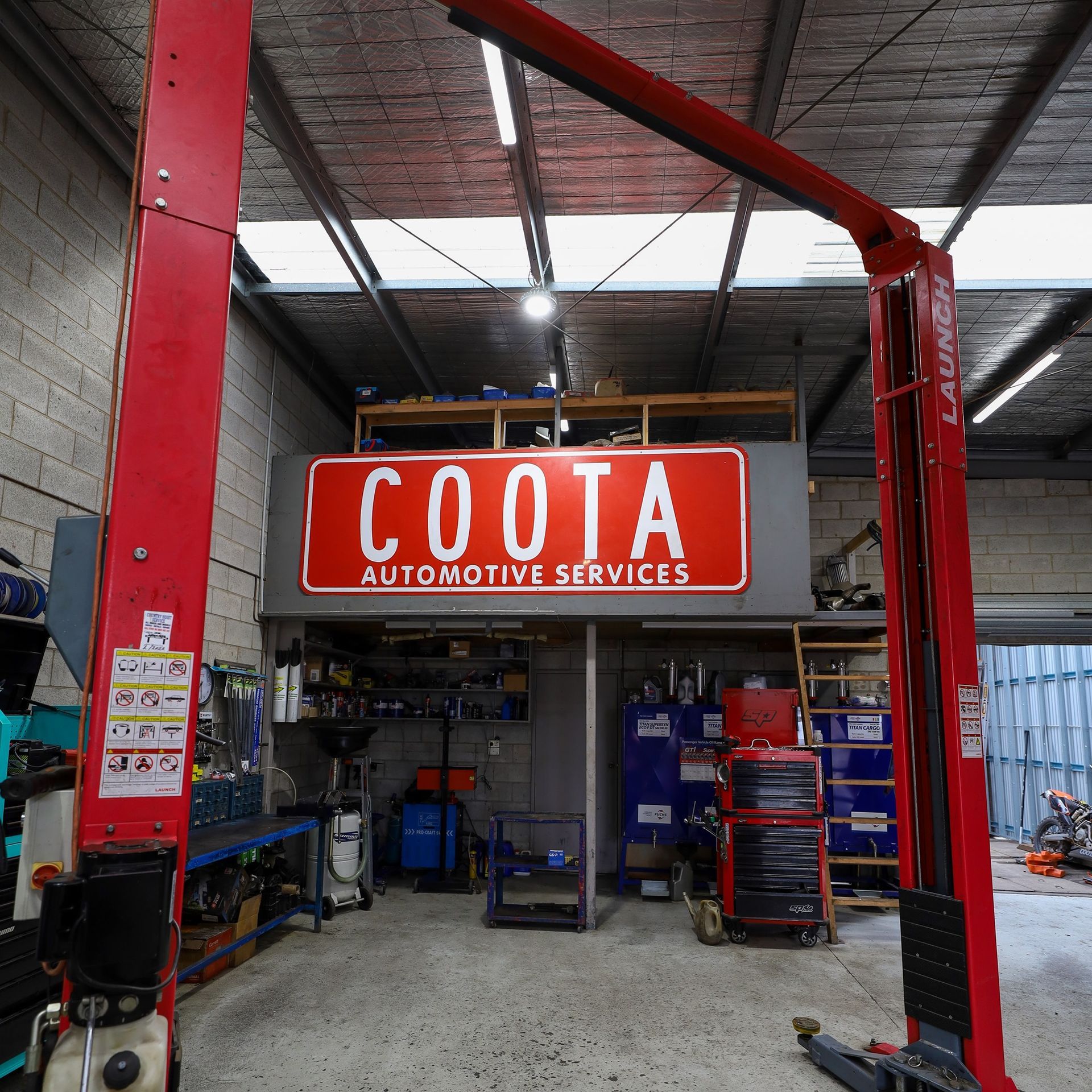 Inside a garage, a red automotive lift. Sign says 