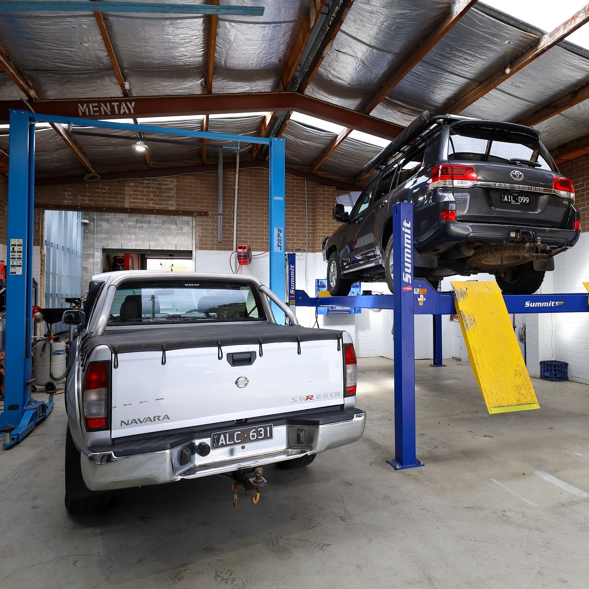 Inside a garage, a white pickup truck and a dark SUV are on lifts. — COOTA Automotive Services in Ballarat East, VIC