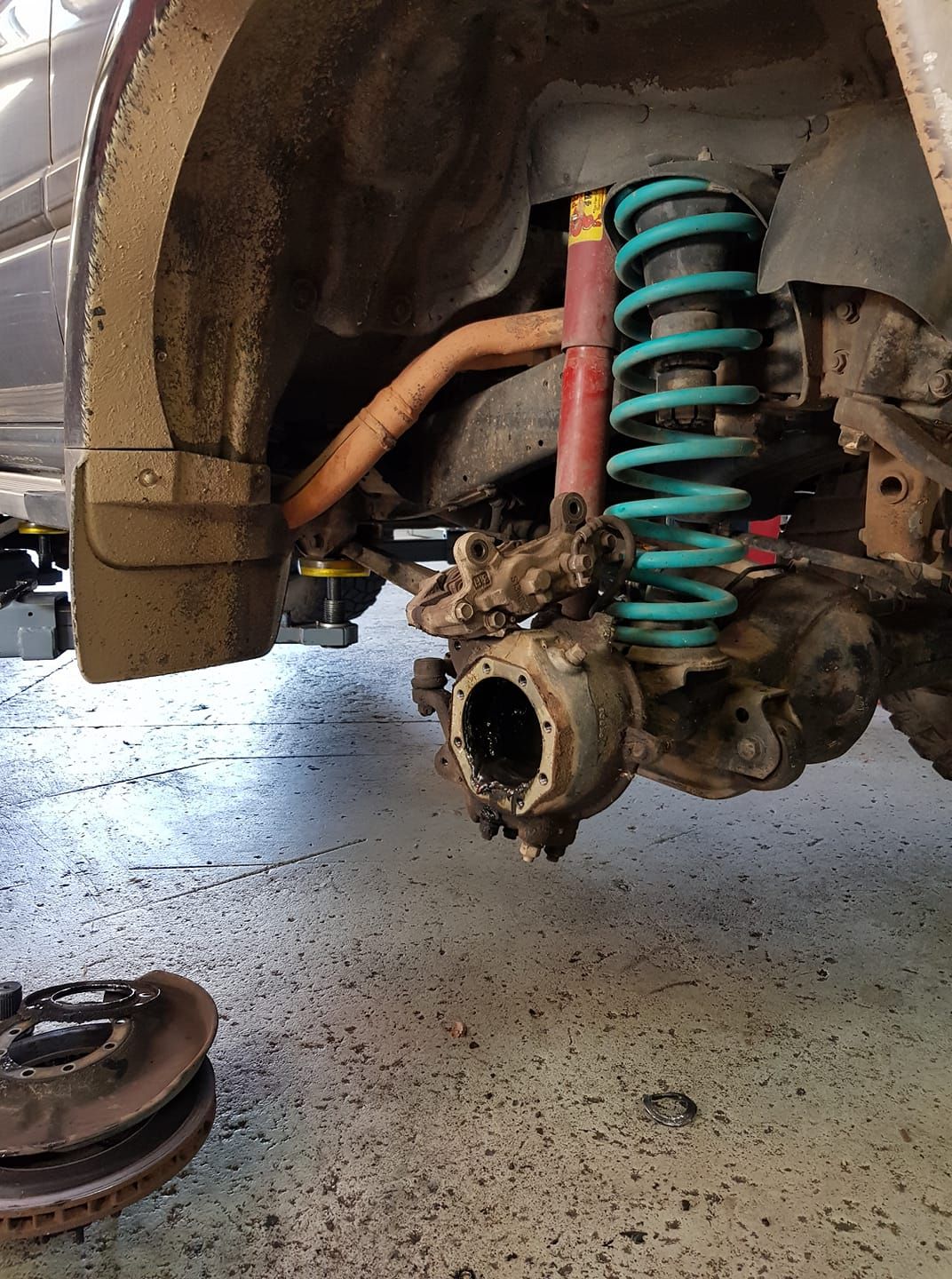 Car suspension system partially disassembled, showing shock absorber, spring, axle, and brake rotor on a shop floor. — COOTA Automotive Services in Ballarat East, VIC