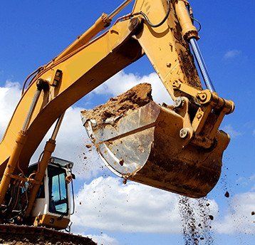 yellow excavator with bucket lifting dirt with blue cloudy sky