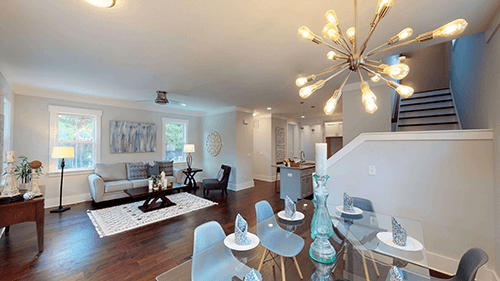 Modern open-plan living space with dining area, sofa, and stairs leading up; bright and airy.