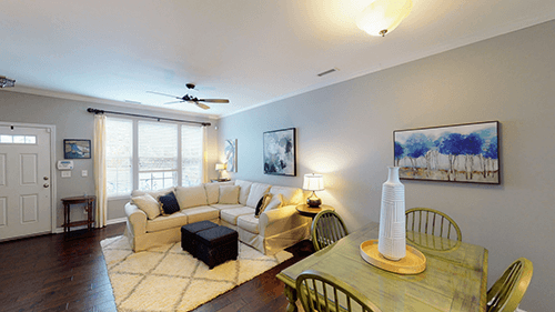 Living room with sectional sofa, dining table, art, and dark hardwood floors.