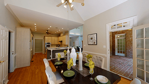 Dining room with table set for a meal, French doors, and a view into a kitchen and outside patio.
