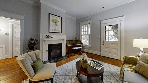 Living room with fireplace, piano, and seating, featuring a neutral color palette and hardwood floors.