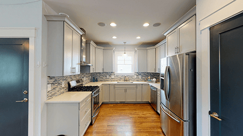 A modern kitchen with light gray cabinets, stainless steel appliances, and a window at the back.