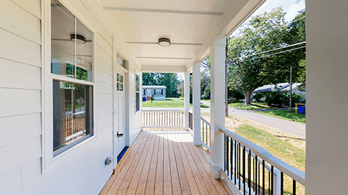 Covered front porch with white siding, wooden deck, and black railing.