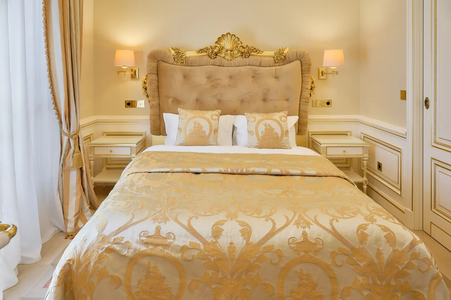 A bed with a gold comforter and pillows in a hotel room.