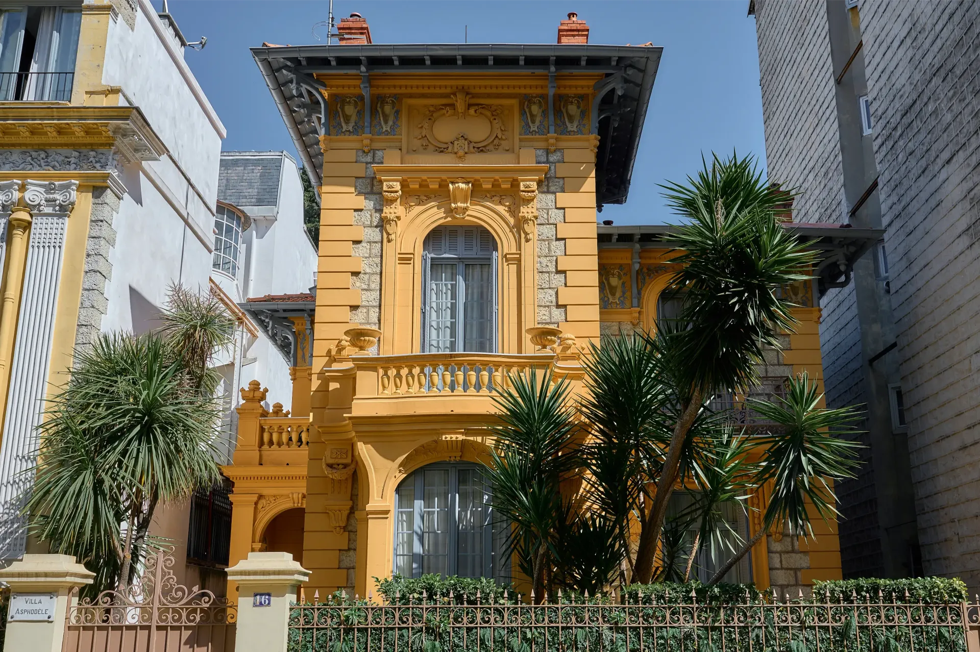 A large yellow building with a balcony and trees in front of it