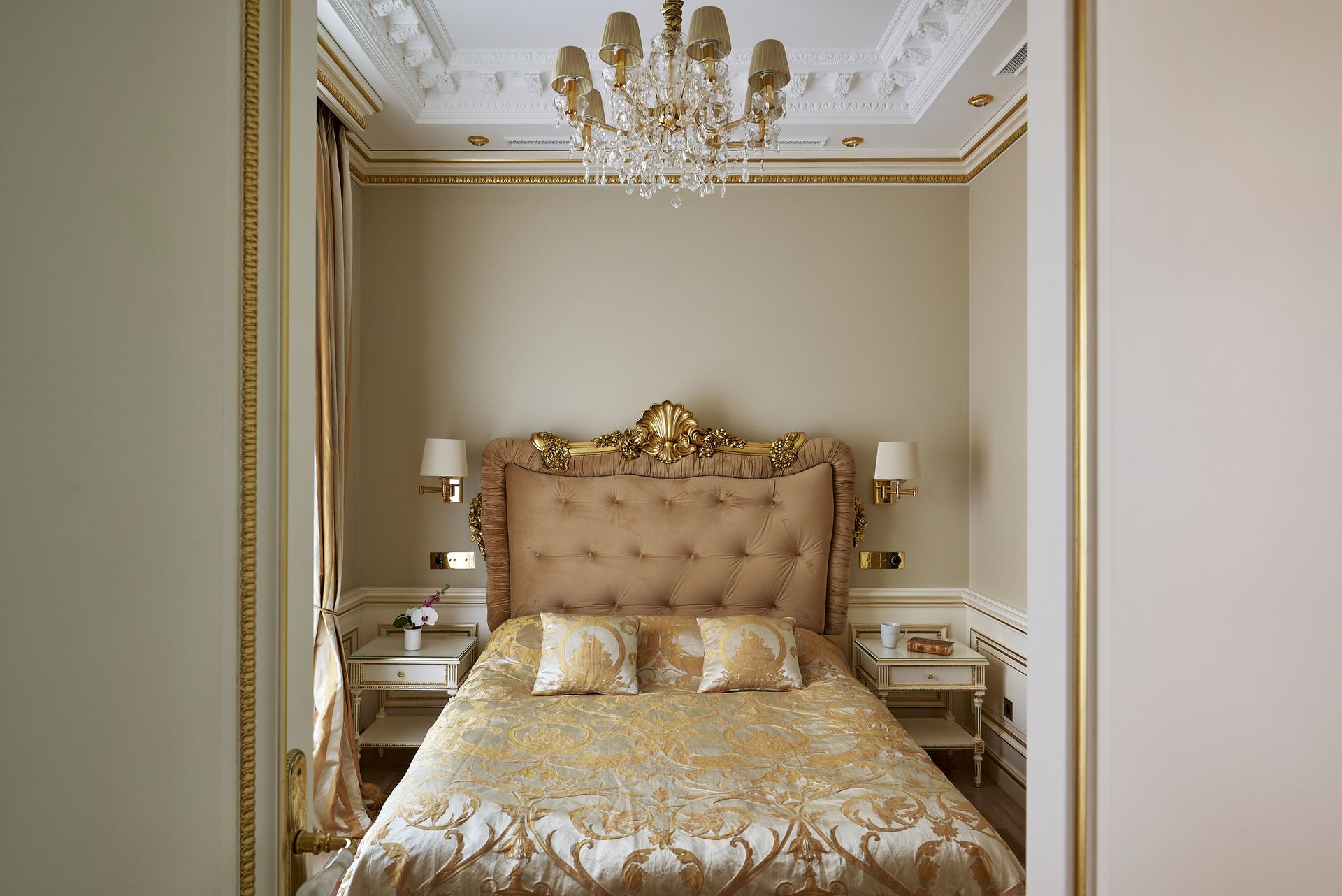 A bed with a gold comforter and pillows in a hotel room.