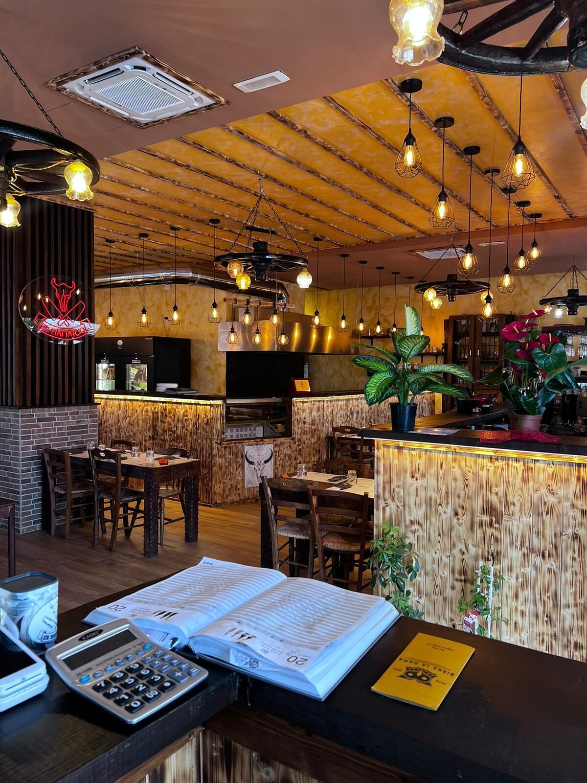 Interno di un ristorante asiatico: tavoli in legno, elementi in bambù, lampade a sospensione, menù aperto sul bancone.