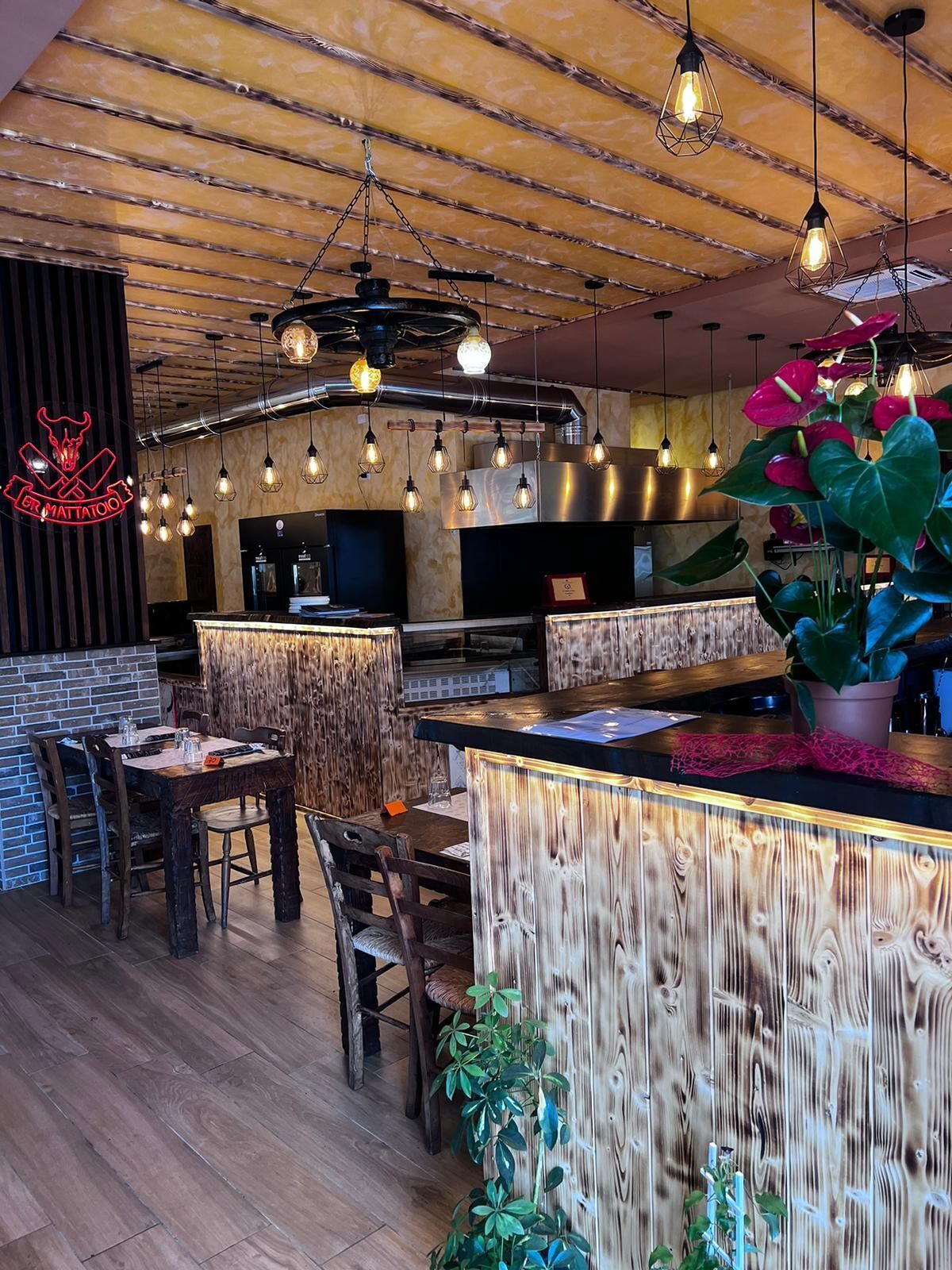 Interno del ristorante con pannelli in legno, tavoli, bar e luci sospese.