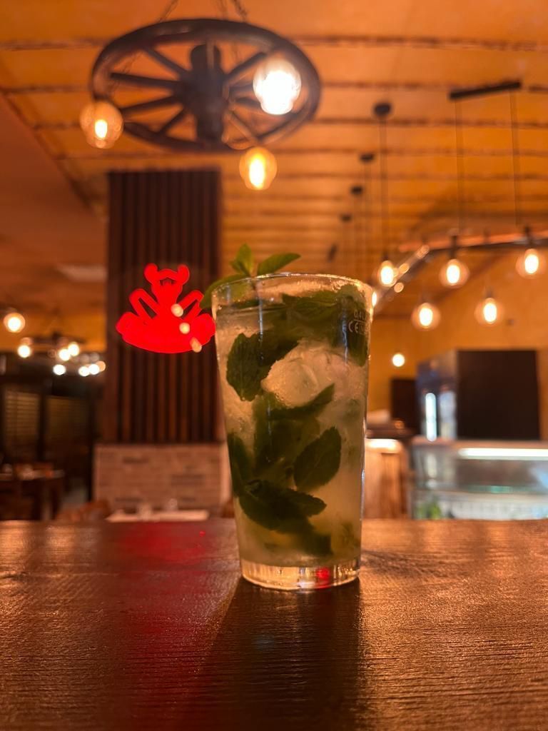 Cocktail Mojito servito sul bancone del bar con foglie di menta e una decorazione rossa sullo sfondo. Illuminazione soffusa.