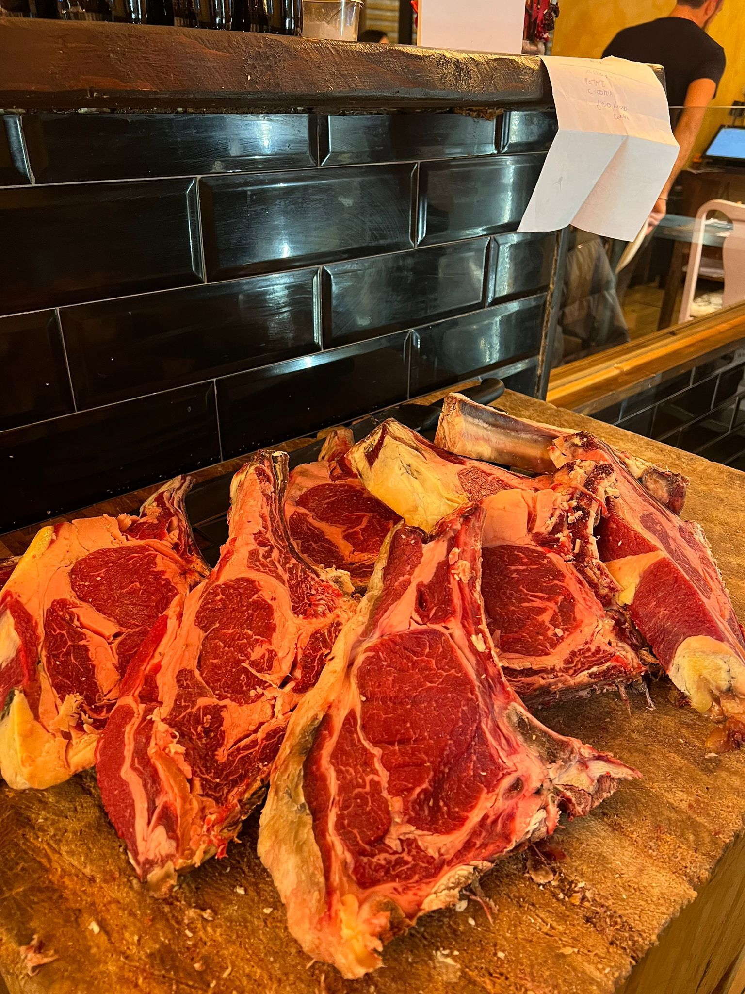 Bistecche di ribeye crude su una superficie di legno, pronte per la cottura, con uno sfondo di mattoni scuri.