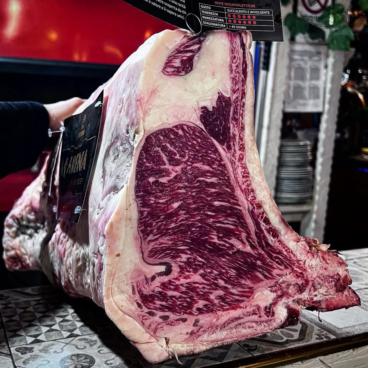 Grande bistecca di ribeye frollata a secco, rossa e marmorizzata, esposta in un ristorante.