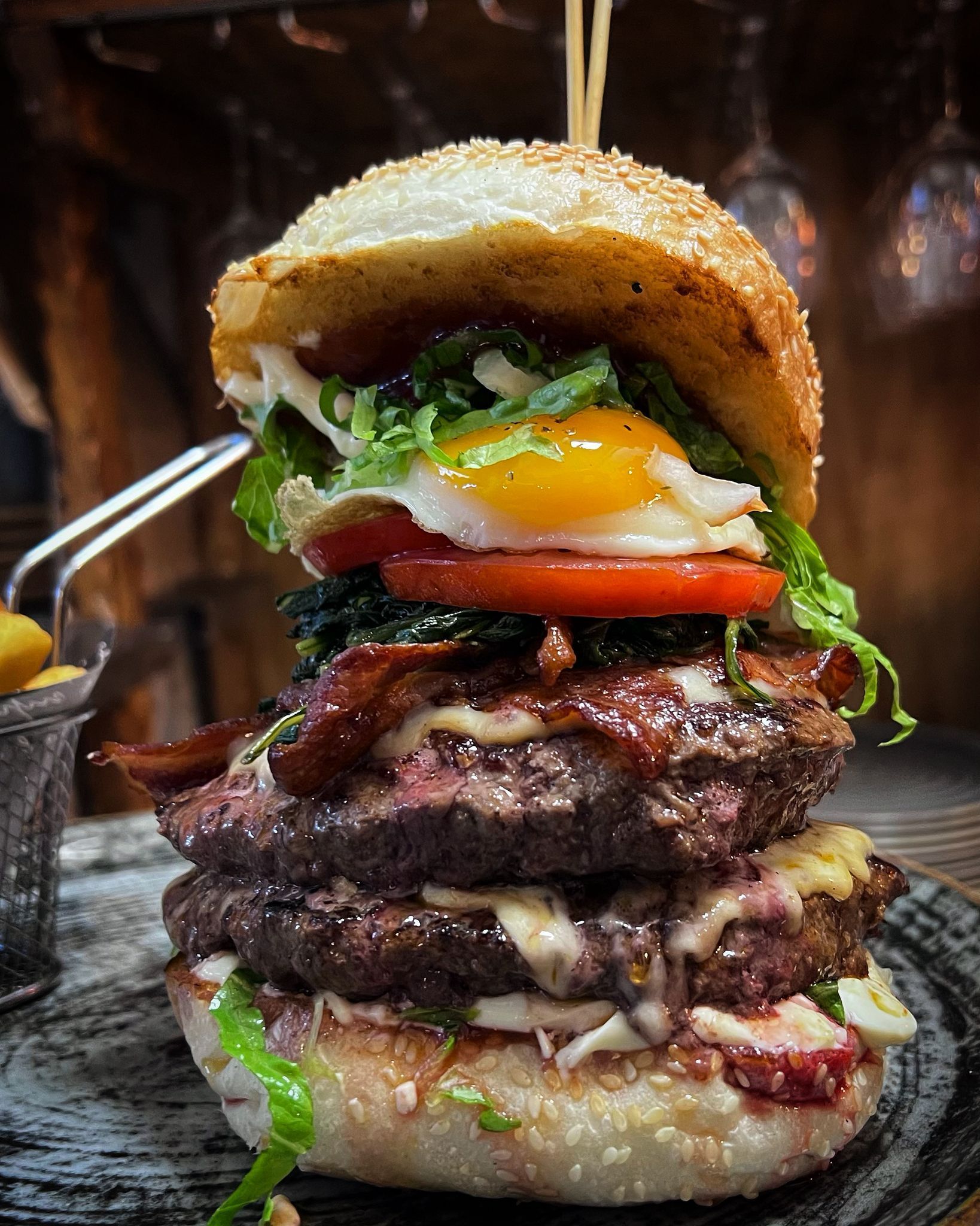 Hamburger a due piani con uovo, pancetta, pomodoro e lattuga, su un panino con semi di sesamo.