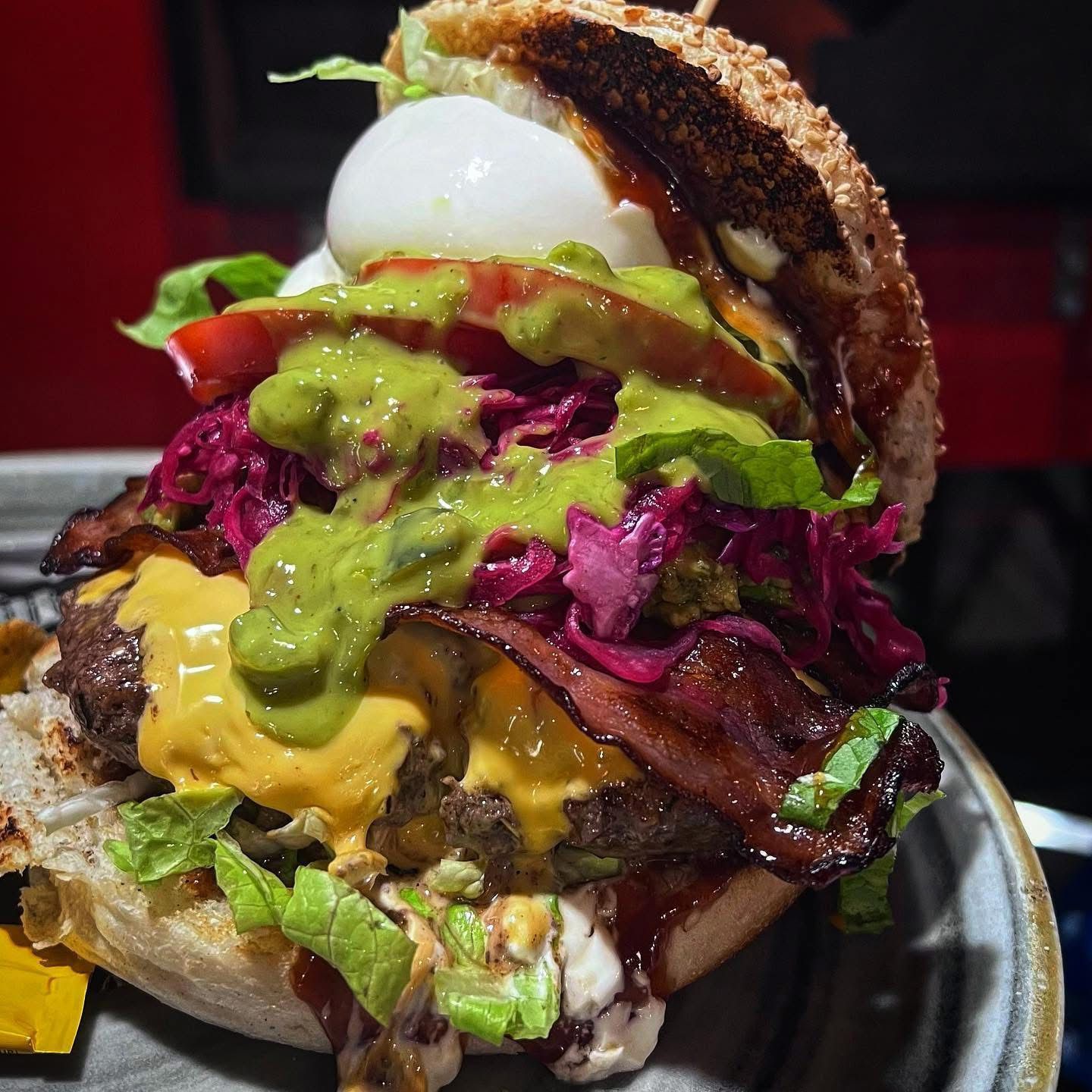 Hamburger con uovo, pancetta, formaggio e salsa di avocado su un panino al sesamo.