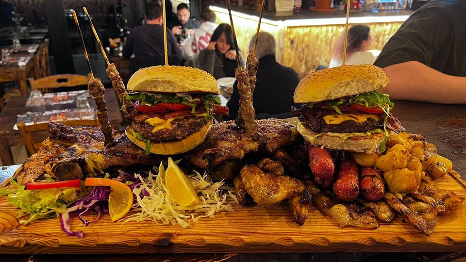 Grande piatto di cibo: hamburger, spiedini, costine, ali di pollo, verdure, limone, tavolo di legno, ristorante.
