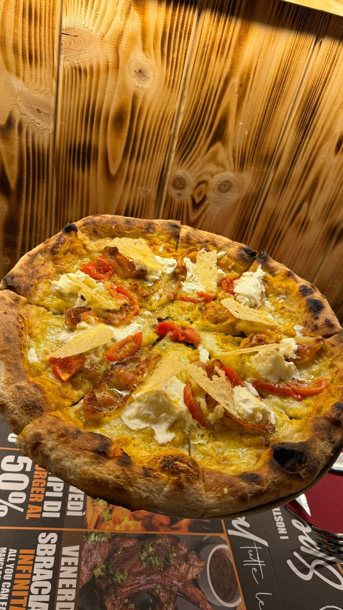 Pizza con formaggio, pomodori e crosta dorata, servita su uno sfondo di legno.