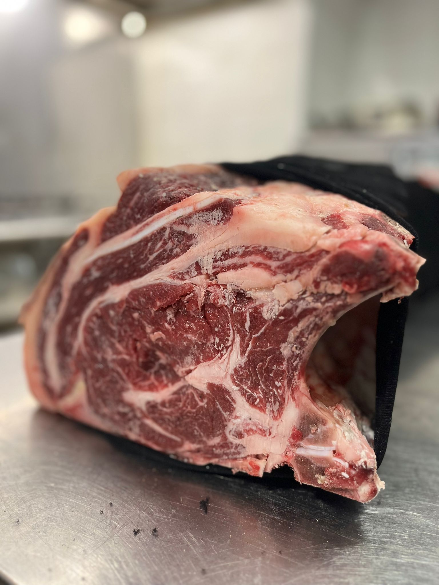 Primo piano di un taglio di carne cruda con l'osso su una superficie metallica, probabilmente una macelleria.