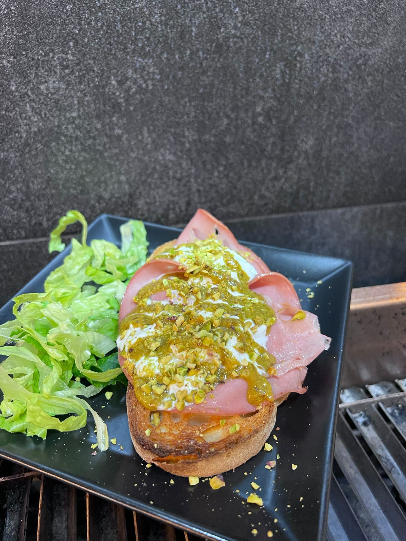 Panino con mortadella, salsa verde e lattuga su un piatto nero.