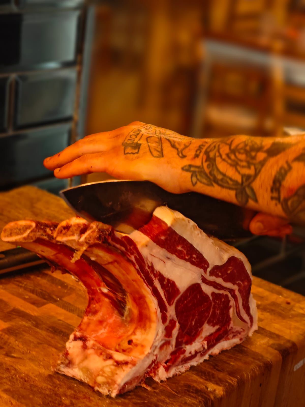 Una grande bistecca cruda su un ceppo da macellaio, una mano tatuata si allunga verso di essa.