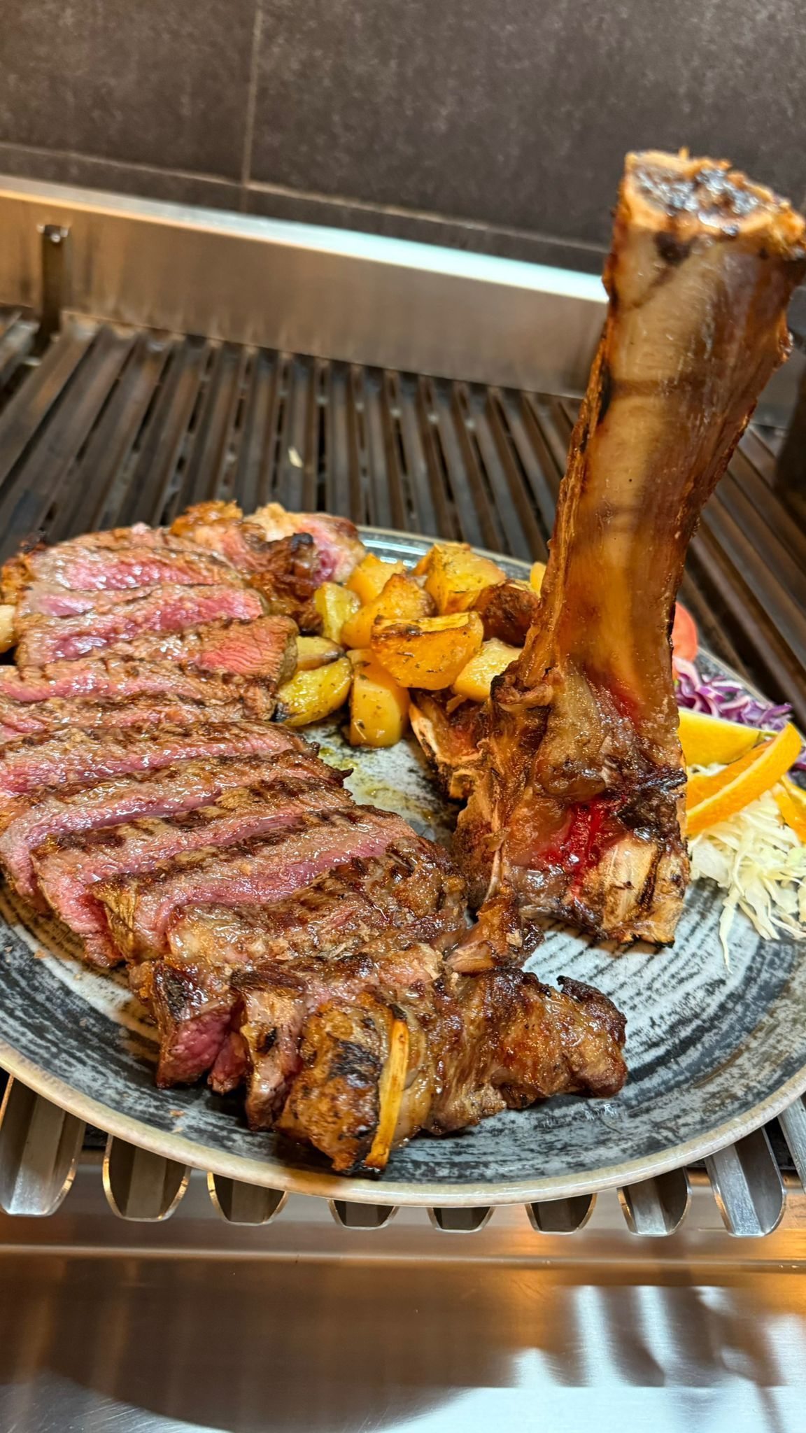 Bistecca alla griglia tagliata a fette con osso, patate e guarnizione su un piatto.