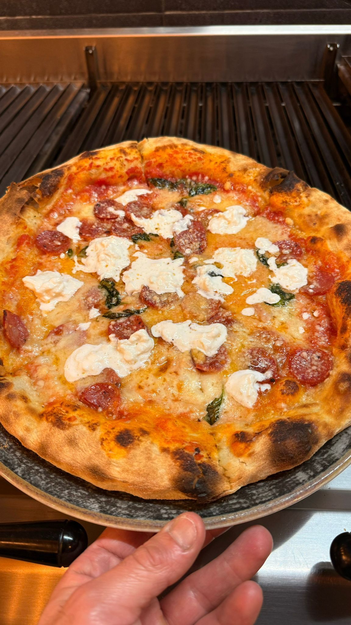 Pizza con formaggio bianco e basilico, servita davanti alla griglia.